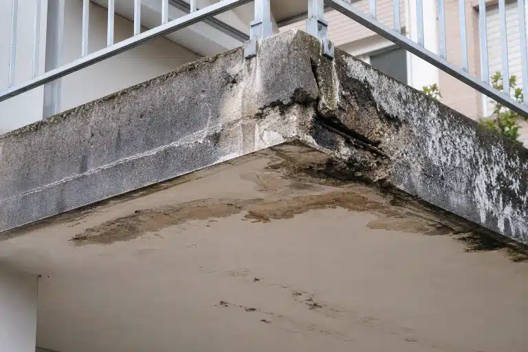 Coin de balcon en béton effrité avec traces d'humidité